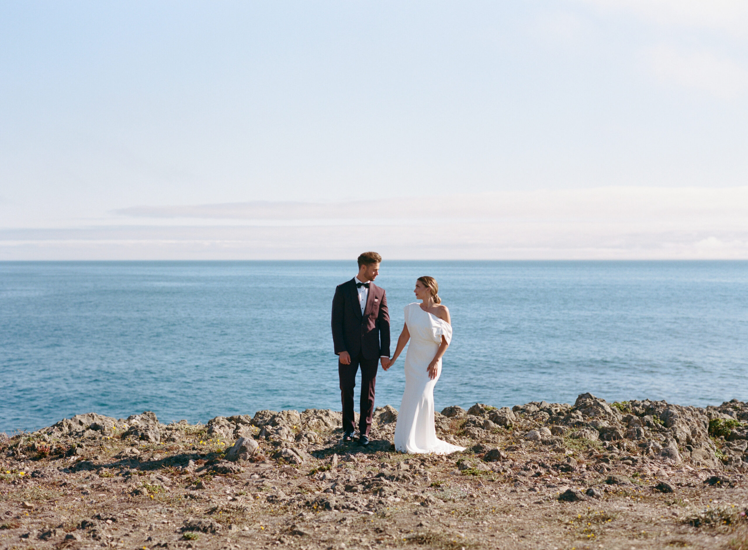 A couple post wedding ceremony standing on the cliffs of Sea Ranch overlooking the ocean after their California elopement